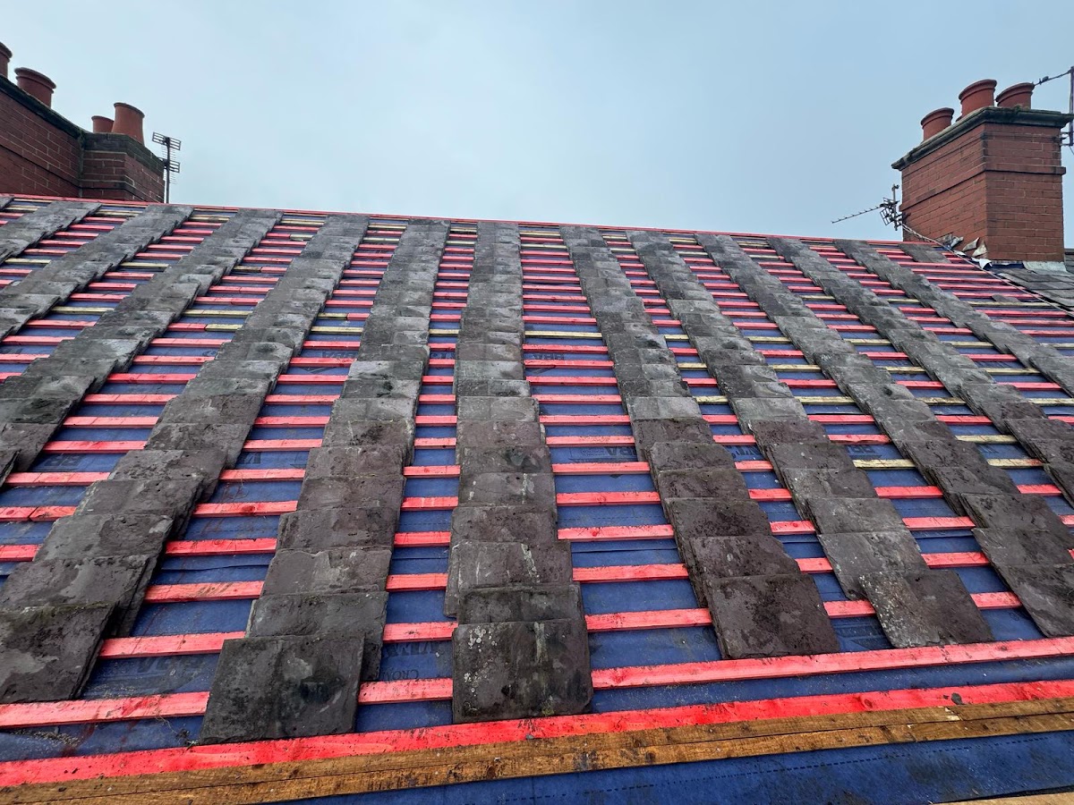A roof mid strip back, with reclaimed slates stacked on new battens over blue breather membrane