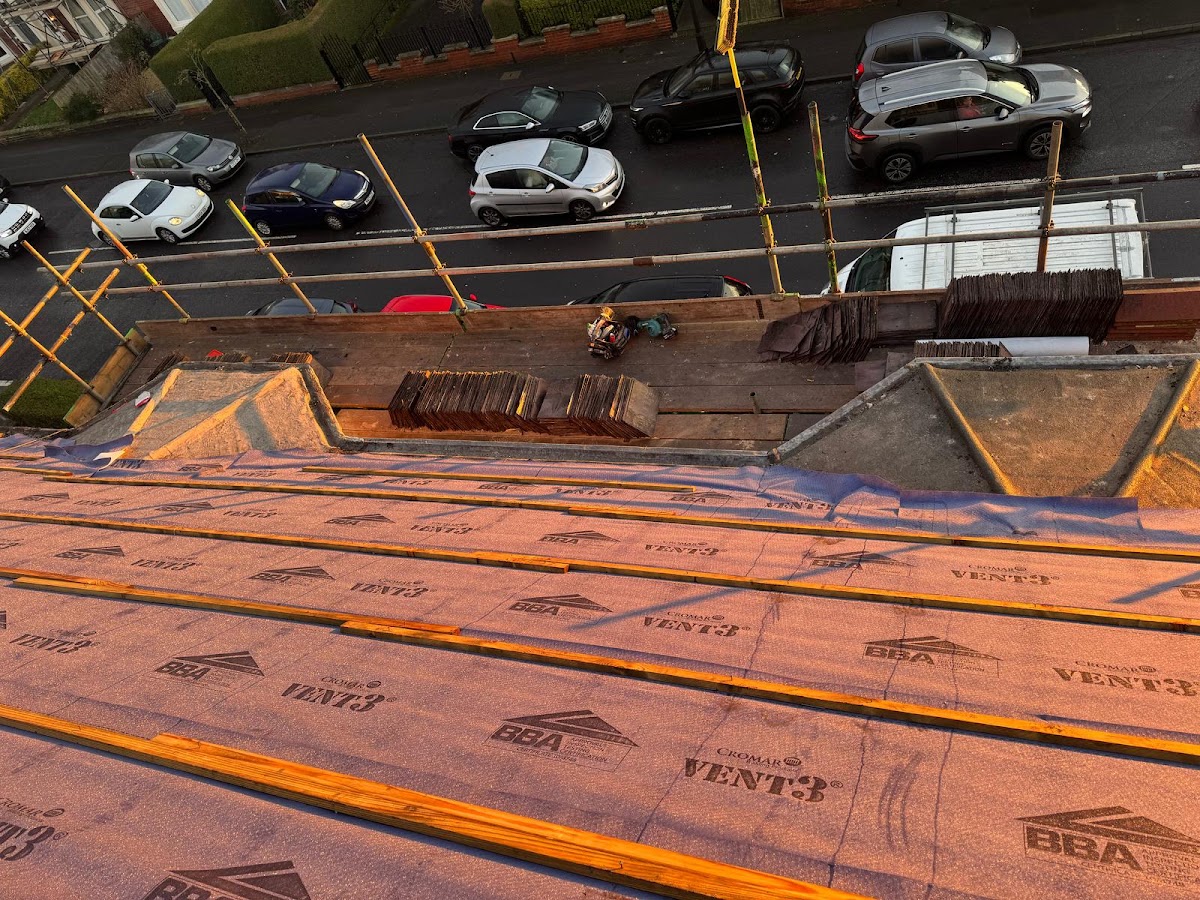 A roof deck covered in breather membrane and battens at golden hour, with the street below